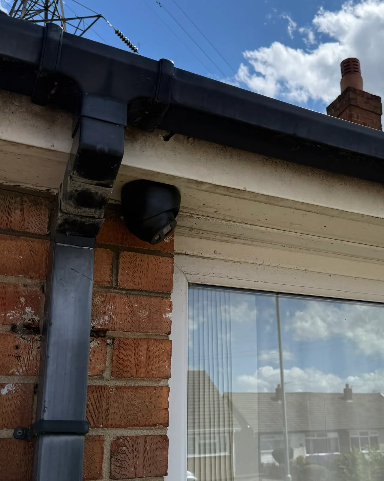 One of Mitu's finished installs: a black Hikvision turret camera under a cream soffit beside the downpipe, brick and fascia clean, no cable anywhere