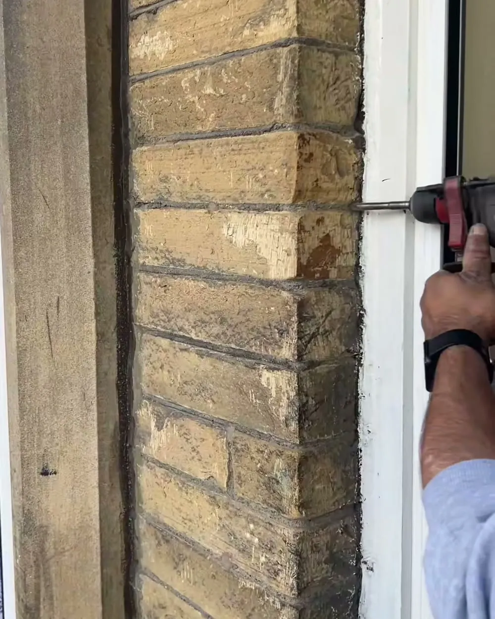A drill bit going into the mortar line on a stone wall, next to a window frame